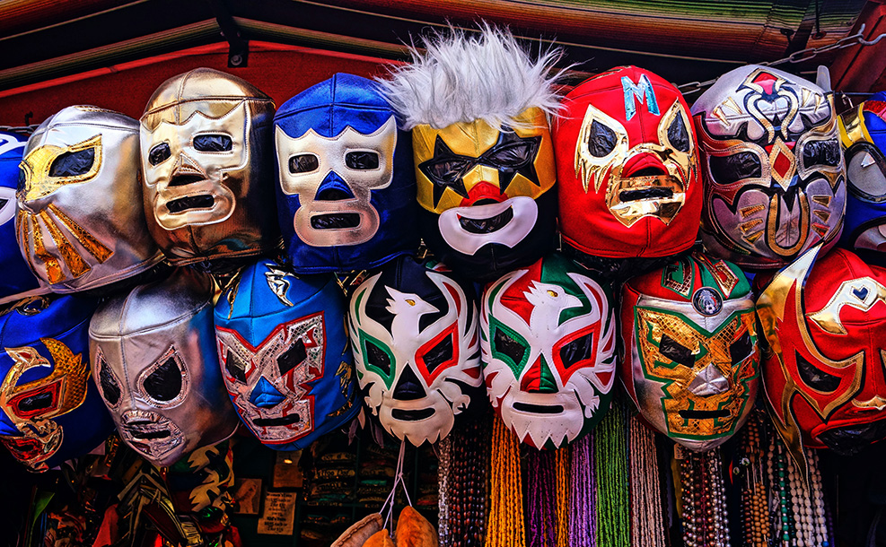 assorted colors and styles of luchador masks hanging on a rod